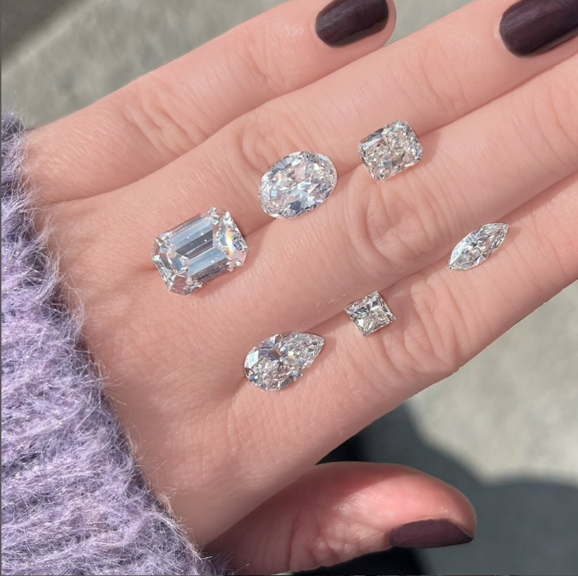 Six diamonds on a hand in various sizes including an emerald cut, oval cut, radiant cut, pear  cut, princess cut, and marquise cut. 