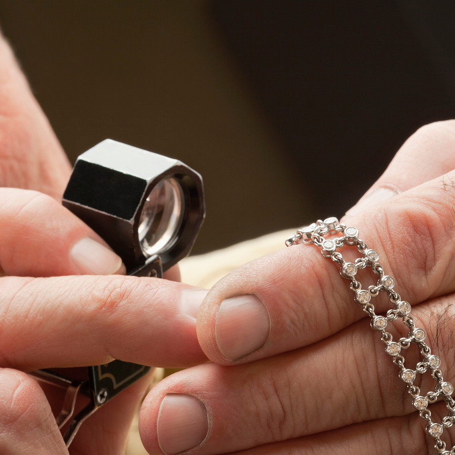 Jeweler's hands holding a loop looking at a diamond bracelet.