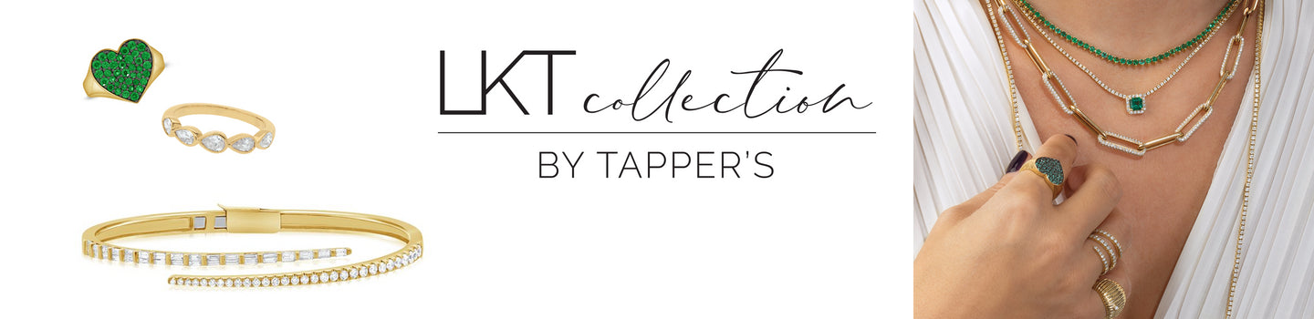 LKT Collection by Tappers, Woman in a white v-neck shirt wearing an emerald tennis necklace, diamond chain necklace with green emerald in the center, paper clip chain necklace with diamonds on each link.