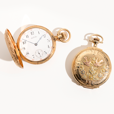Two gold pocket watches on a white background