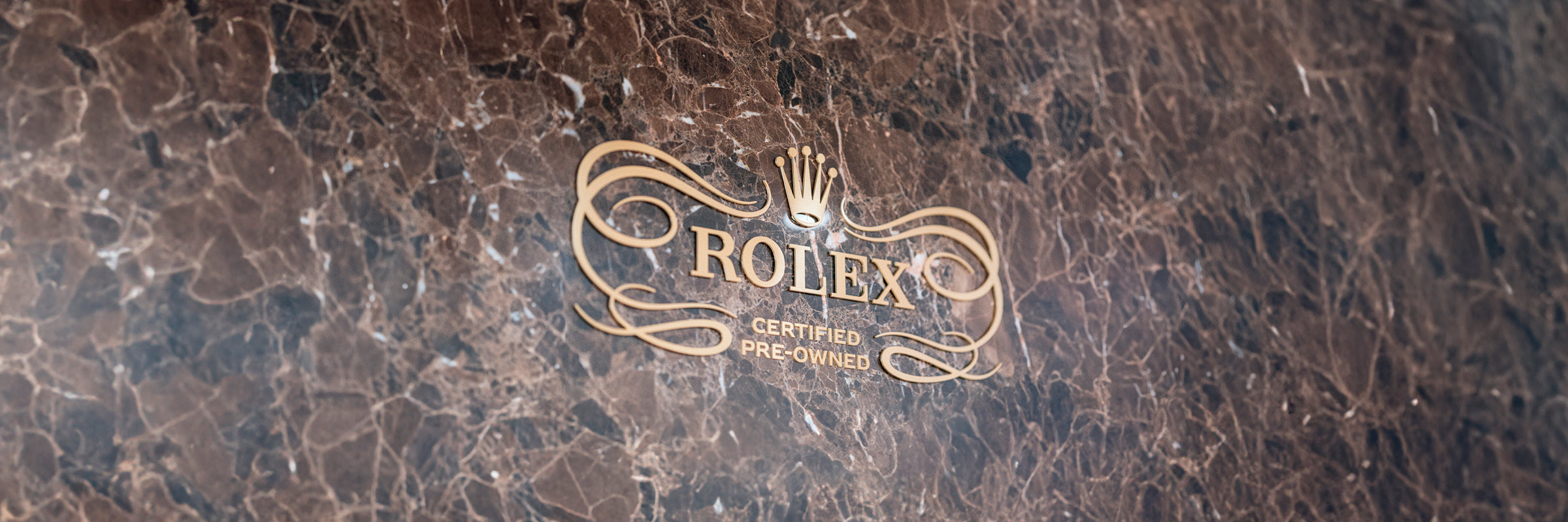 Gold Rolex Certified Pre-Owned logo engraved on a brown marble wall.