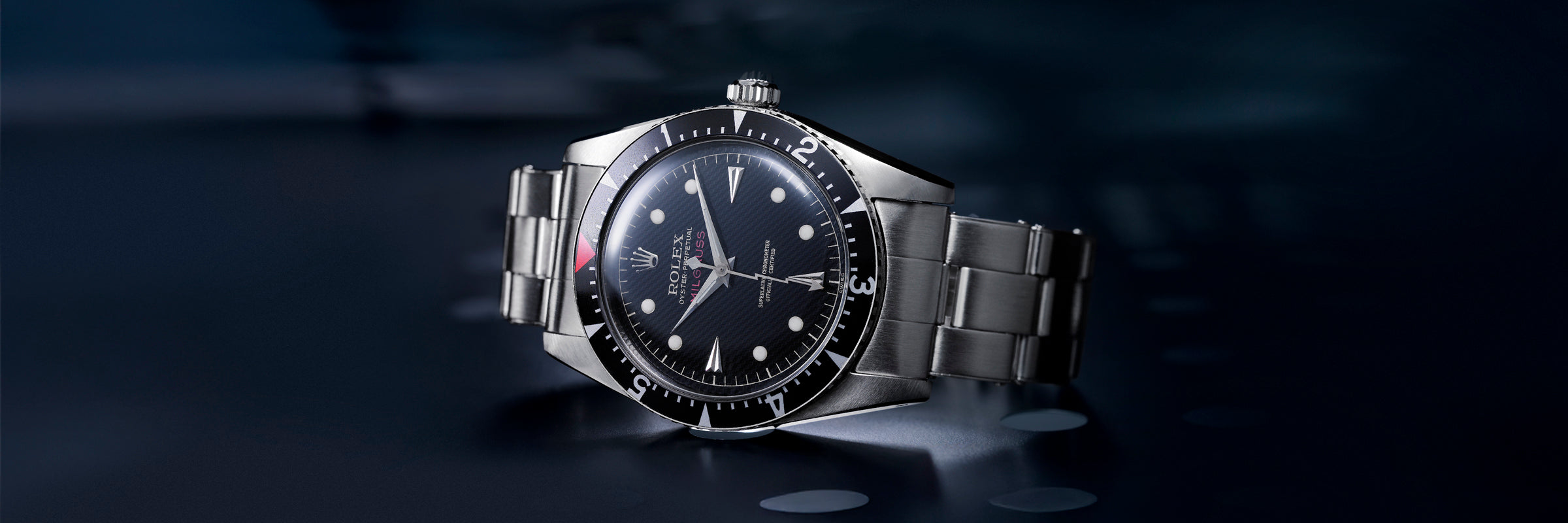 Vintage Rolex Milgauss watch with black dial and rotating bezel, displayed at an angle on a dark blue background.