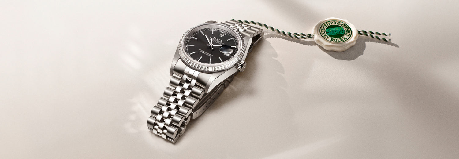 Stainless steel Rolex Datejust wristwatch with black dial and Jubilee bracelet, displayed beside a certified pre-owned Rolex tag on a light background.