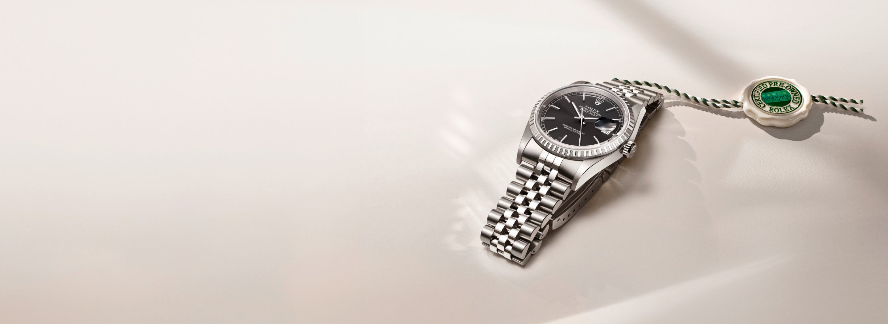 Stainless steel Rolex Datejust wristwatch with black dial and Jubilee bracelet, displayed beside a certified pre-owned Rolex tag on a light background.