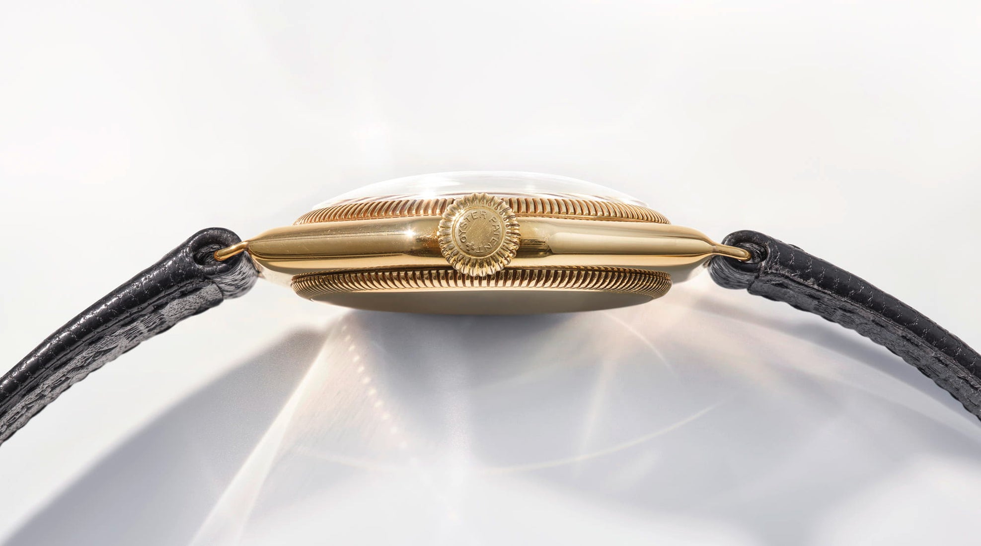 Gold bracelet with black strap on a white background