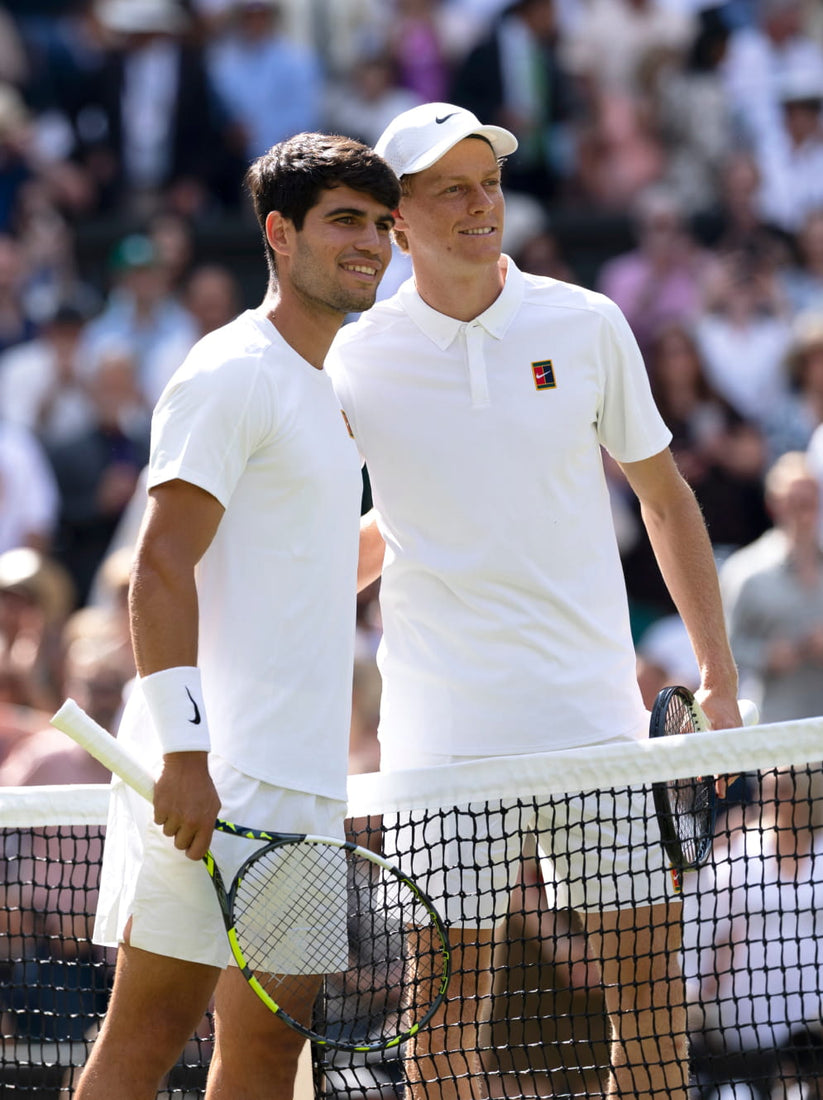Two tennis players in white uniforms standing behind a net with a blurred crowd in the background